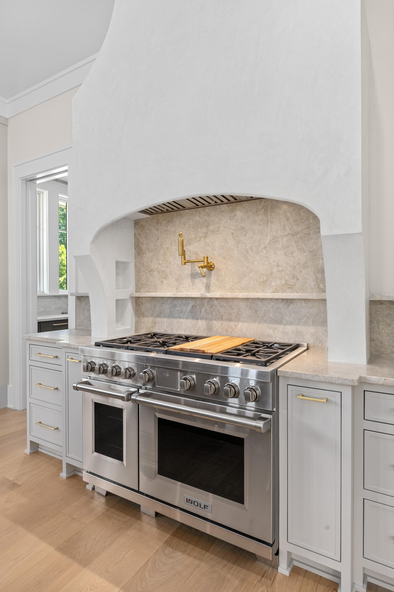 Chef's kitchen with a stainless Wolf 48-inch dual-fuel range under a curved plaster hood, a marble backsplash, and a brass pot-filler