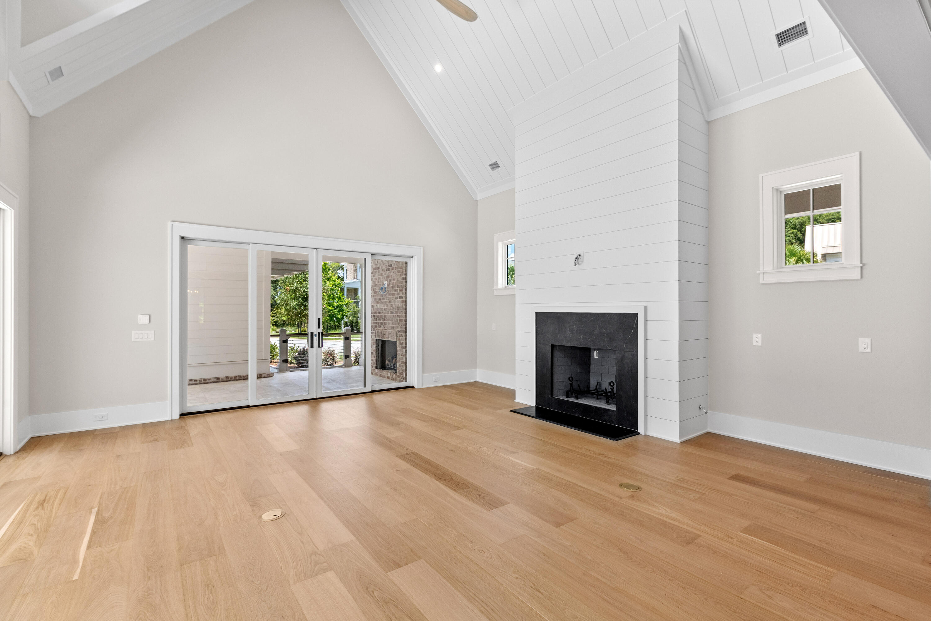 Vaulted great room with a white shiplap fireplace, white oak floors, and a wall of glass doors opening to the covered porch