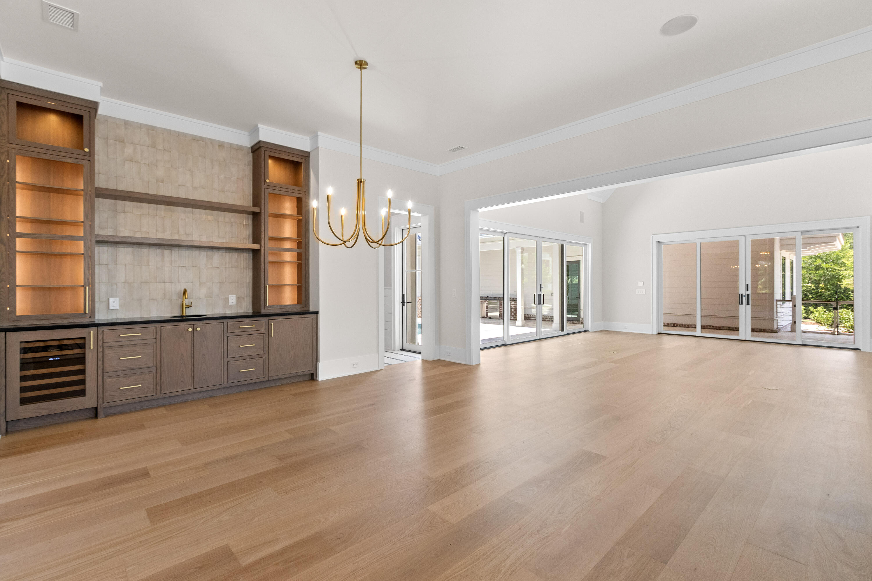 Wet bar with walnut cabinetry, a wine fridge, and a brass chandelier, opening into the great room and its wall of glass doors at 221 Black Powder Lane