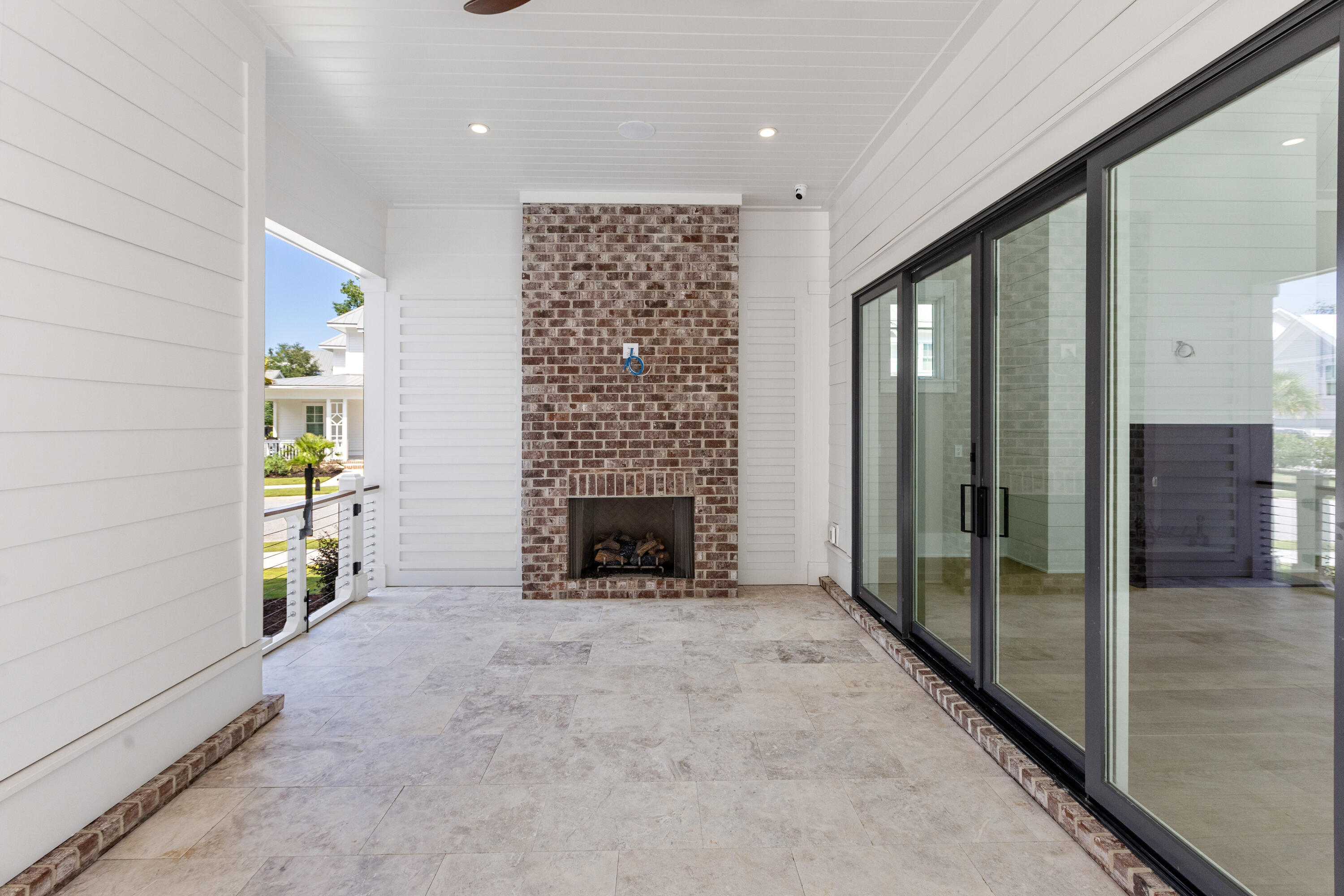 Covered porch with a brick wood-burning fireplace, a white oak plank ceiling, travertine floors, and sliding glass doors to the interior