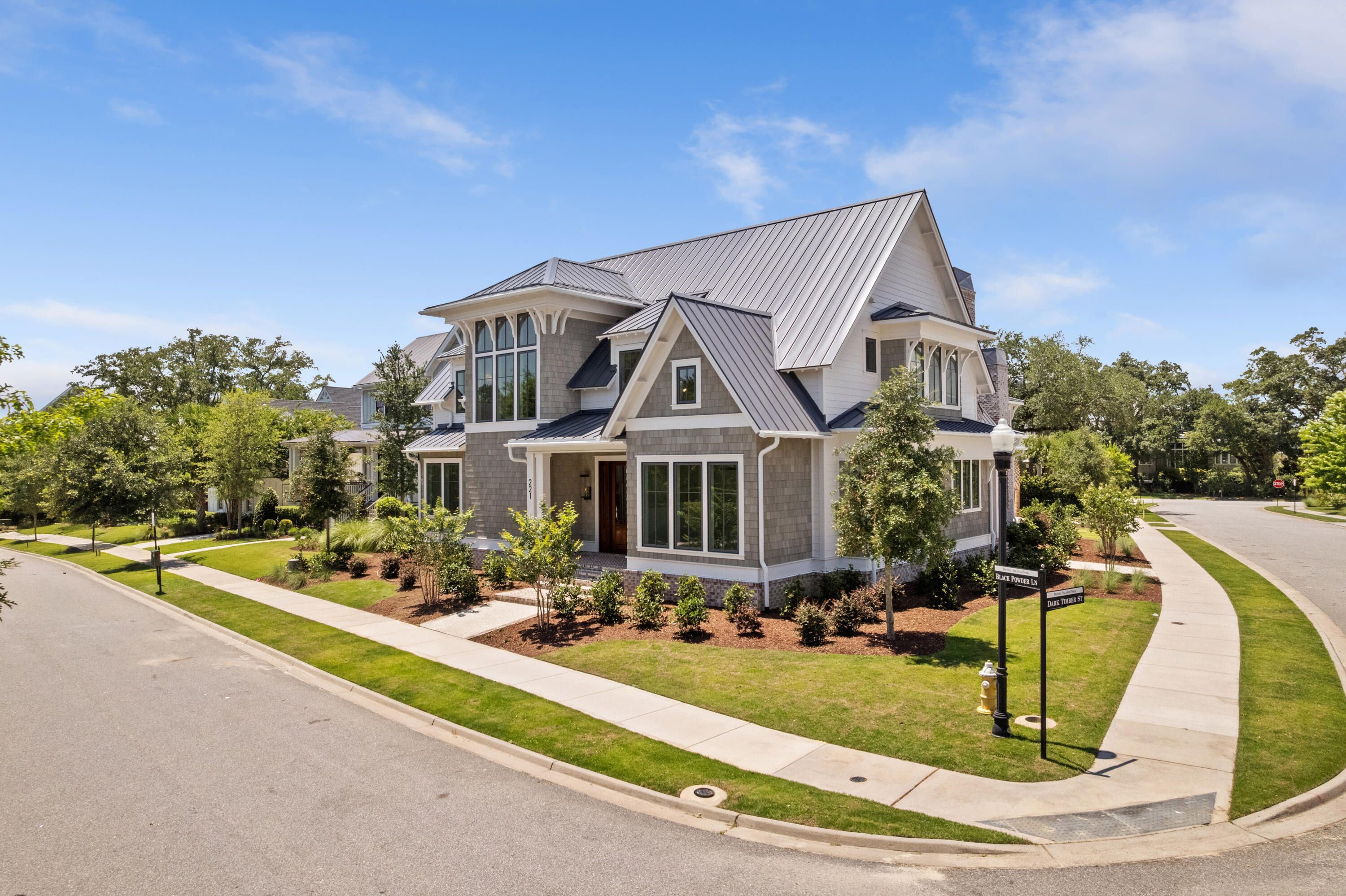 Corner-lot exterior of 221 Black Powder Lane, a new grey-shingle Lowcountry estate with a standing-seam metal roof, mahogany front door, and landscaped lawns on Daniel Island